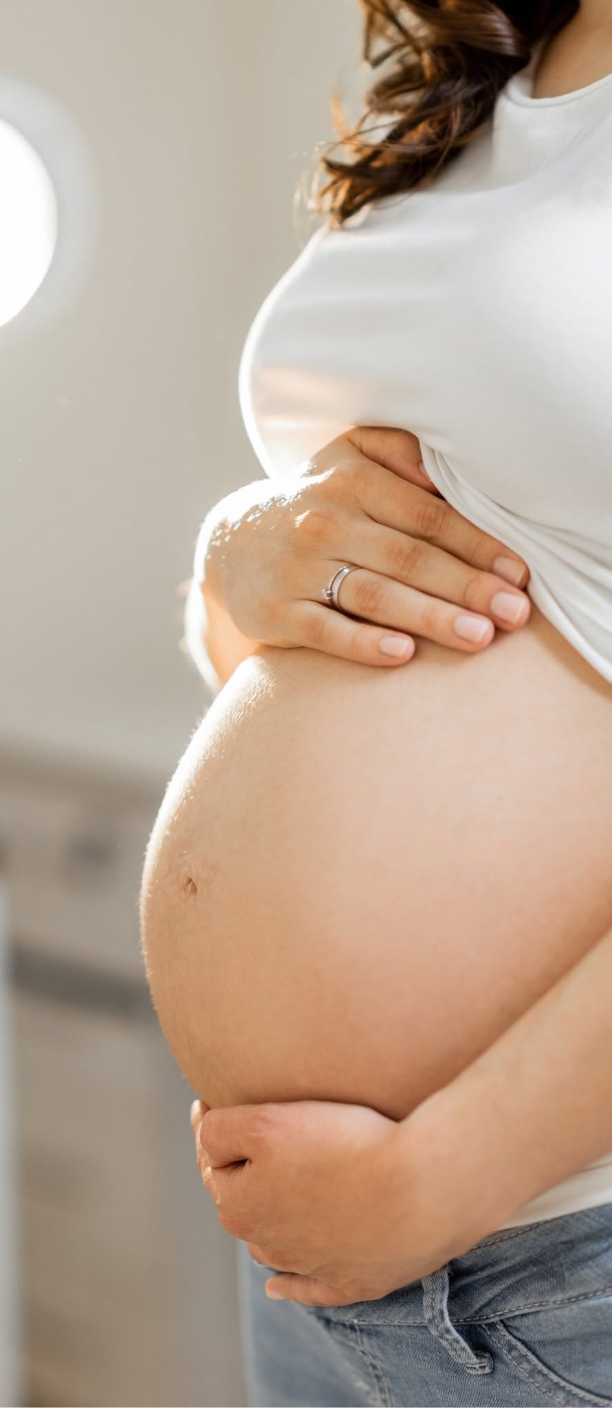 An expecting mother gently holding her belly in soft natural light, illustrating prenatal massage care